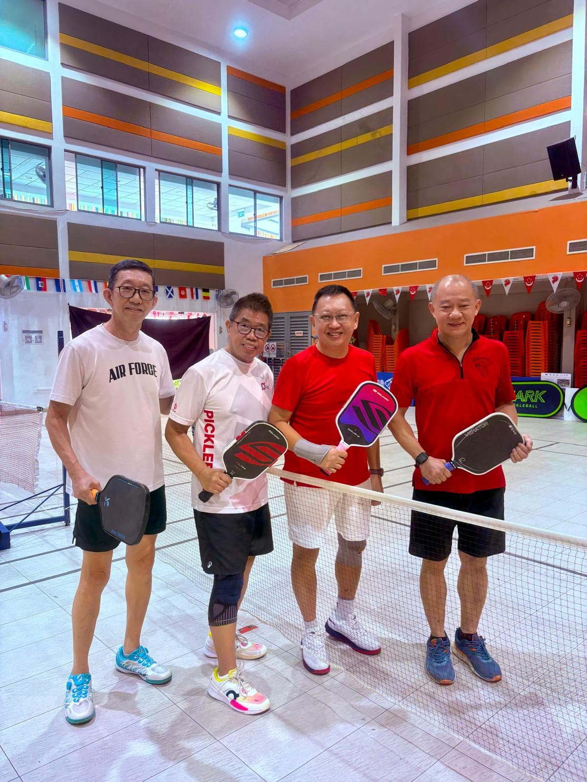Four players pose at the net holding their paddles between games.