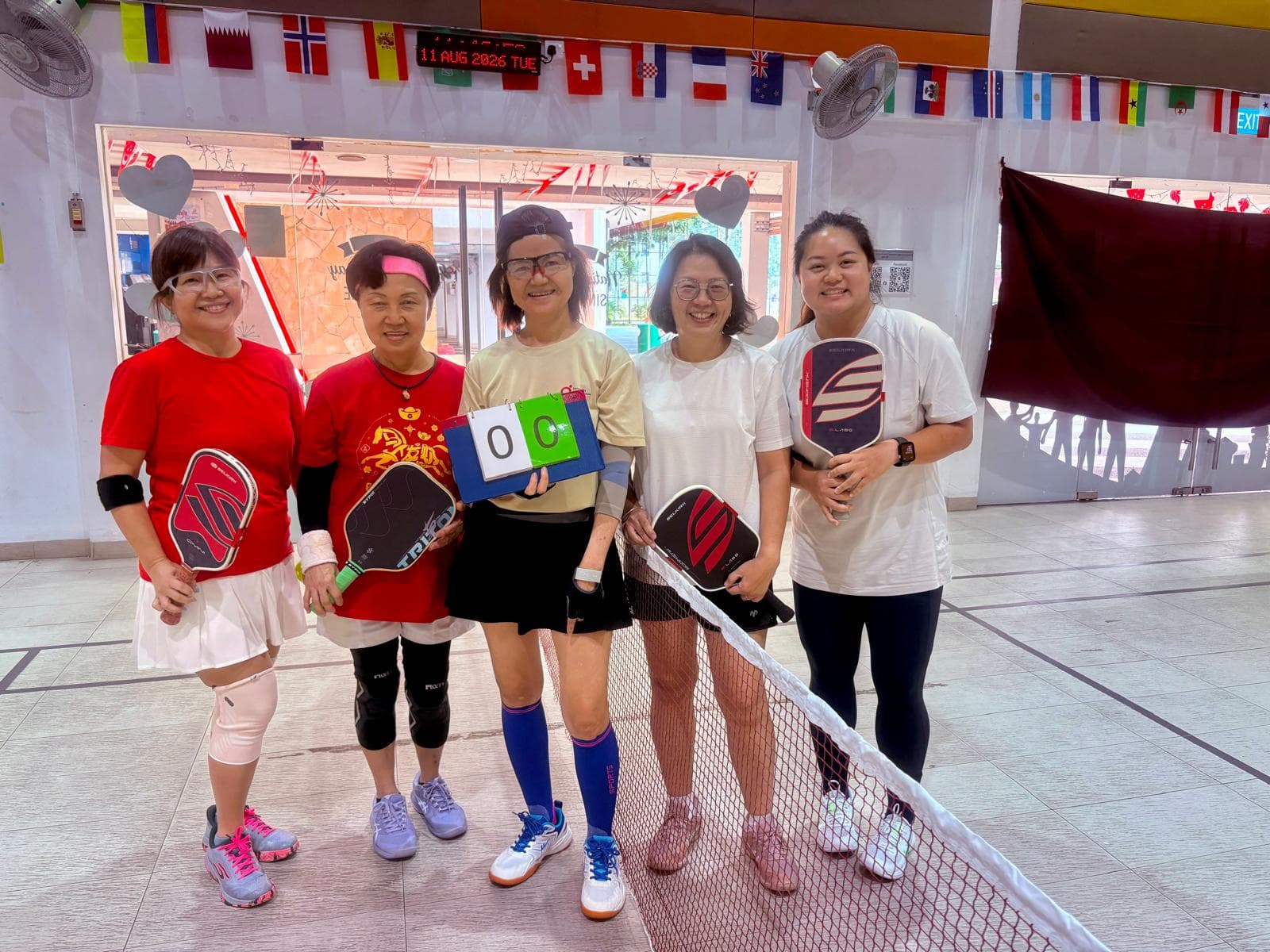 A team of women players pose at the net before a match, National Day bunting overhead.